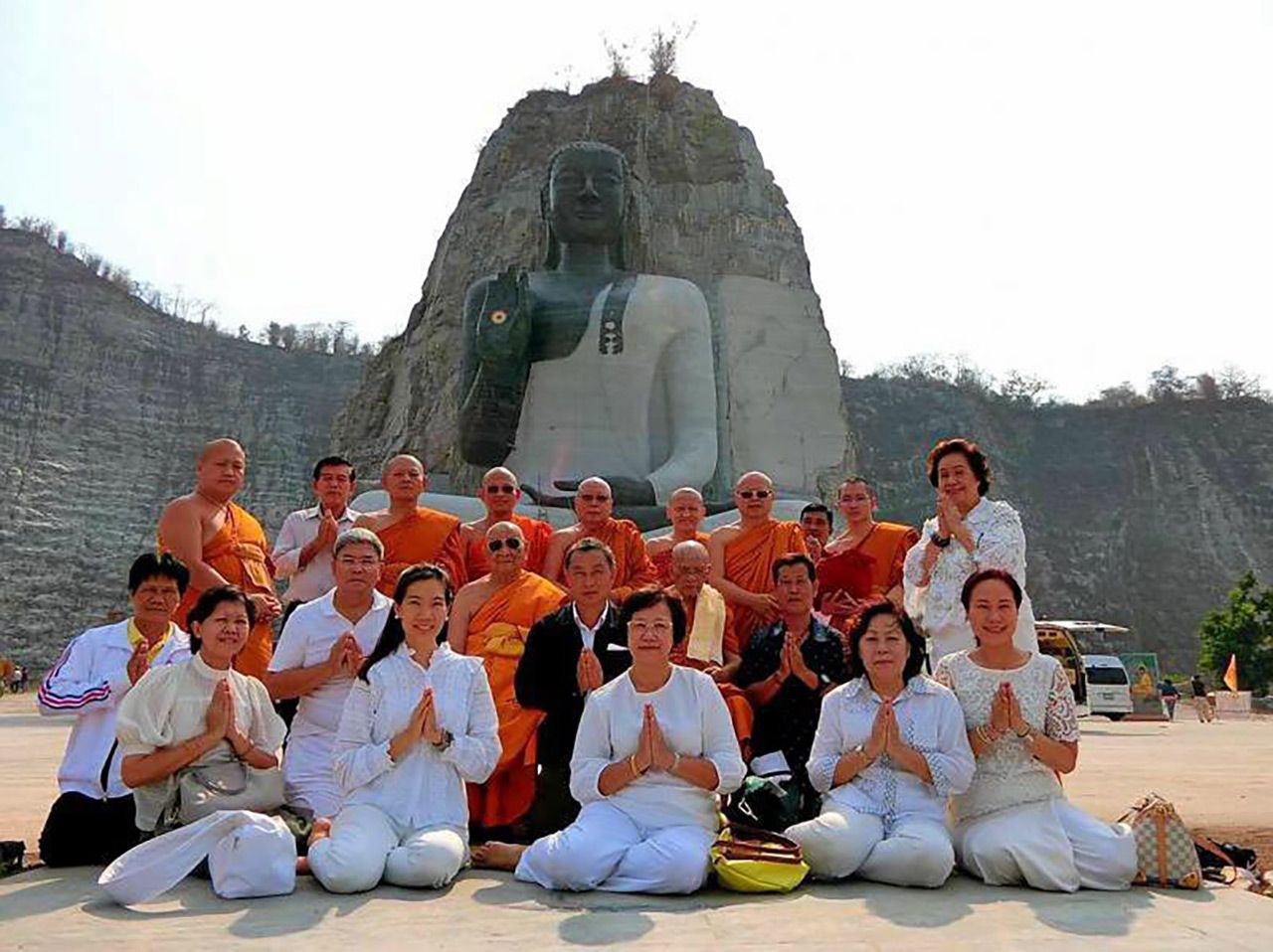 พุทธศาสนิกชนที่ไปร่วมปฏิบัติธรรมและทำบุญ ถ่ายภาพกับพระสงฆ์หน้าพระแกะสลักหน้าผาใหญ่ที่สุดในประเทศไทย.