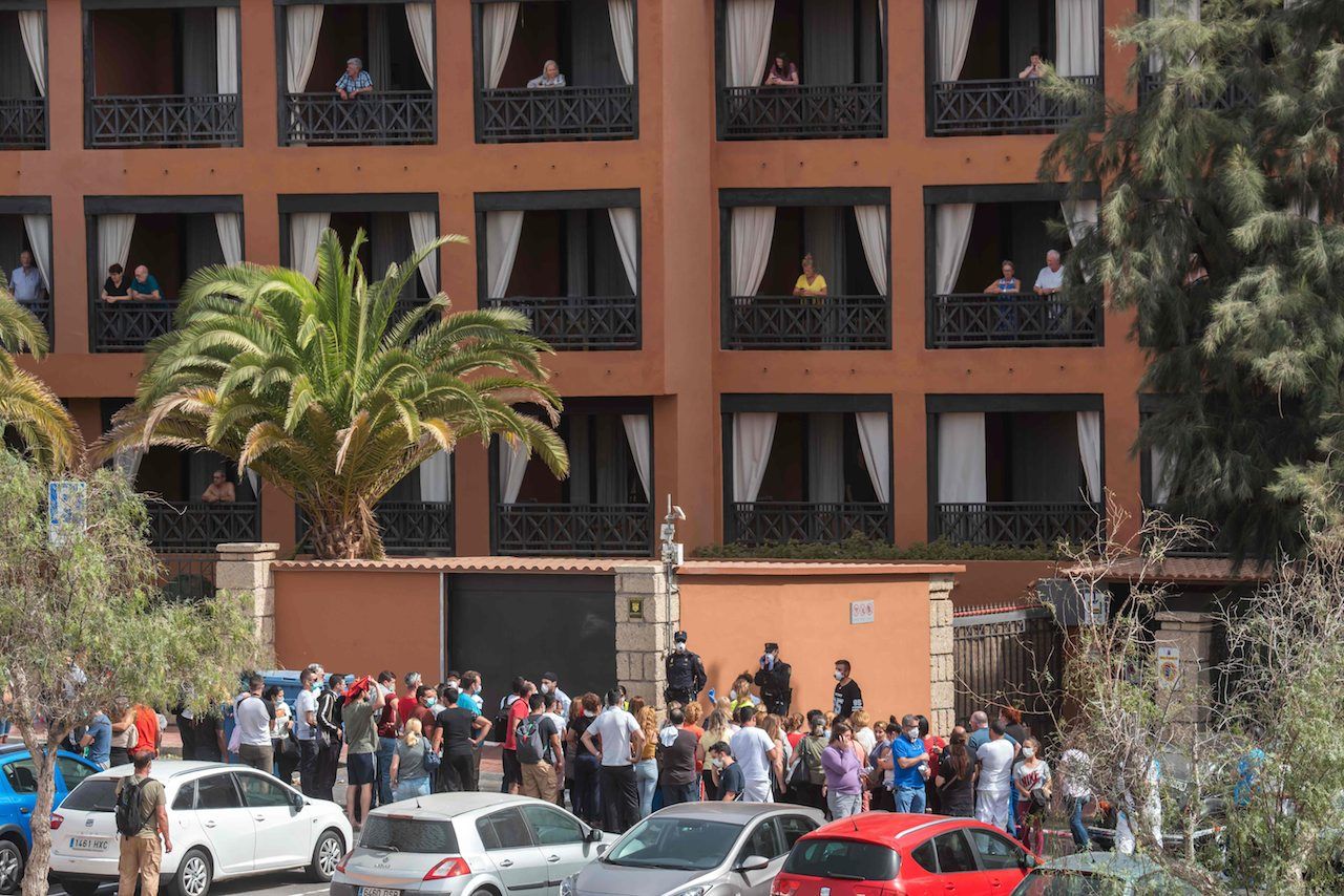 นักจิตวิทยาพูดคุยกับคนงานหน้าโรงแรม เอช10 คอสตา อาเดเช พาเลซ ขณะที่แขกของโรงแรมเฝ้ามองลงมาจากหน้าต่างห้องตัวเอง