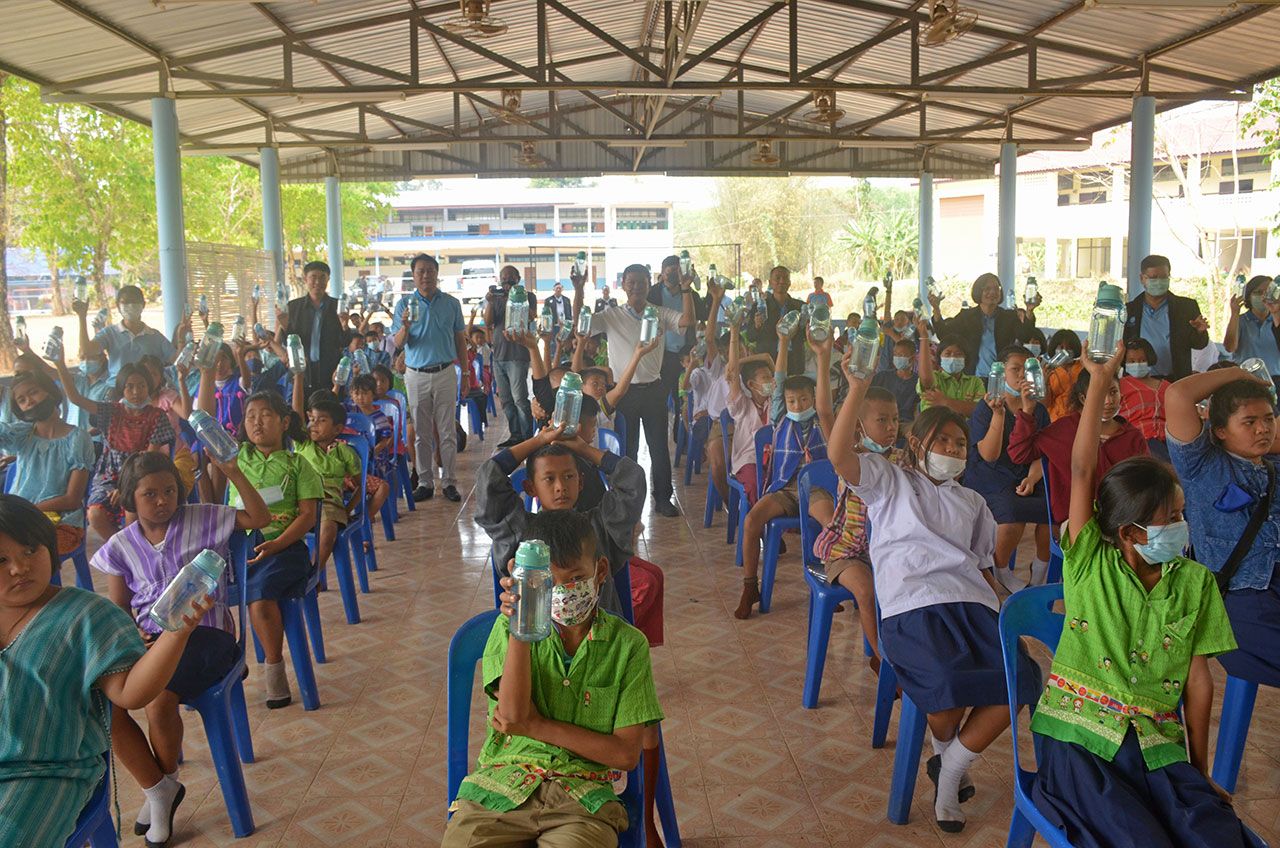 เด็กนักเรียน ร.ร.วัดหินดาด นั่งรอรับสมุด ดินสอ รองเท้า และอุปกรณ์การเรียนที่ กปน.นำไปมอบให้ โดยเว้นระยะห่างตามมาตรการป้องกันโรคไวรัสโควิด-19.