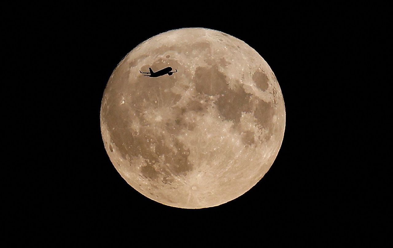 เครื่องบินแล่นผ่านซุปเปอร์บลูมูนที่น่านฟ้าเหนือกรุงลอนดอน ประเทศอังกฤษ