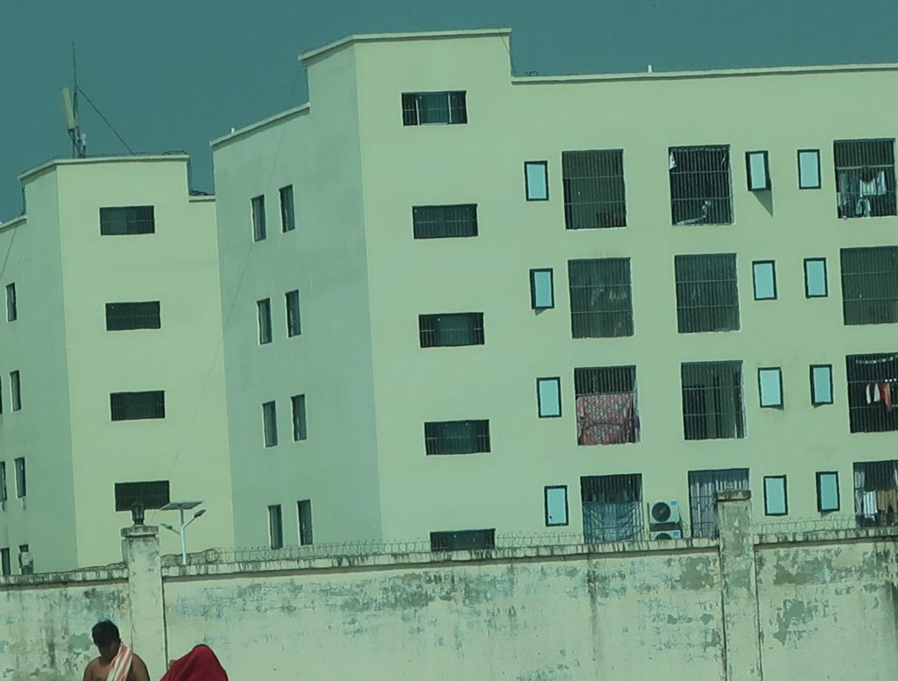 หน้าต่างที่มีการติดลูกกรง ด้านหลังกำแพงสูงของอาคารแก๊งคอลเซ็นเตอร์ โดยมีลวดหนามหรือลวดหนามสามชั้นภาพ: Amnesty International