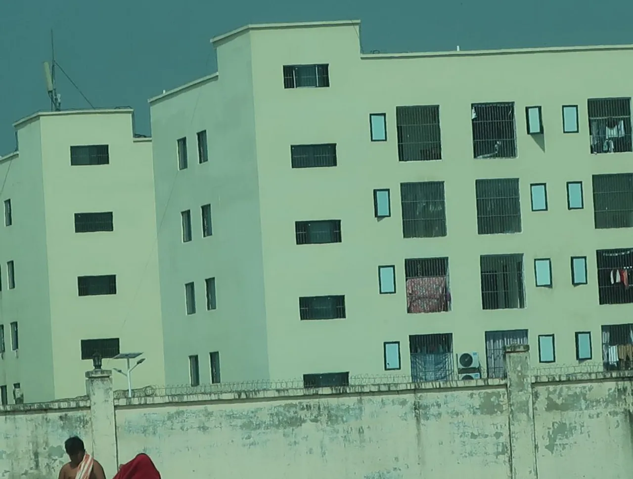 หน้าต่างที่มีการติดลูกกรง ด้านหลังกำแพงสูงของอาคารแก๊งคอลเซ็นเตอร์ โดยมีลวดหนามหรือลวดหนามสามชั้นภาพ: Amnesty International