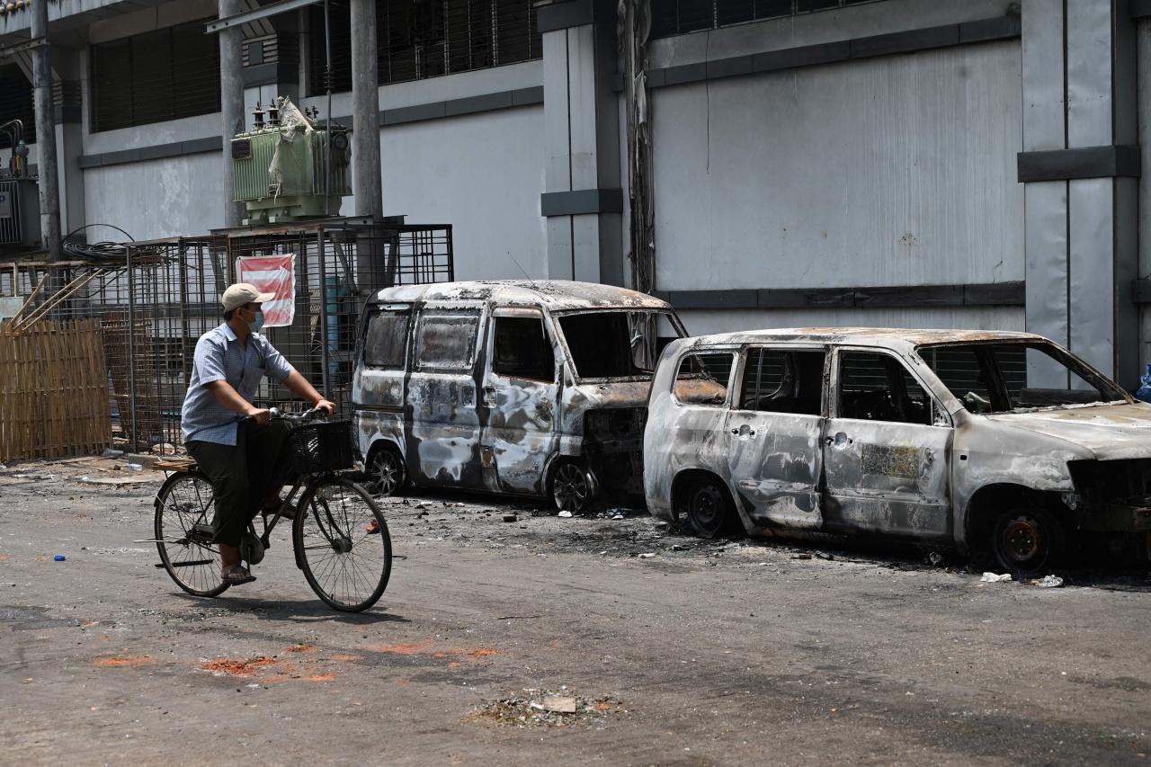 Villagers ride bicycles through the wreckage of cars that were burned during the protests.