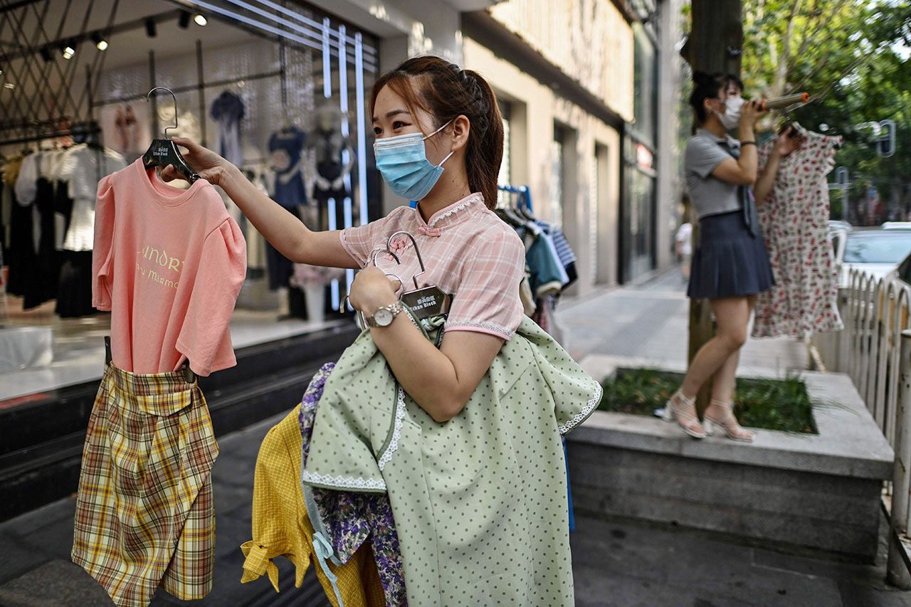 กลับสู่ปกติ พนักงานขายของร้านจำหน่ายเสื้อผ้าเมืองอู่ฮั่น จีน ถือเสื้อผ้า เชิญชวนลูกค้าที่หน้าร้านตามปกติ หลังหมดปัญหาโควิด-19 ระบาด.