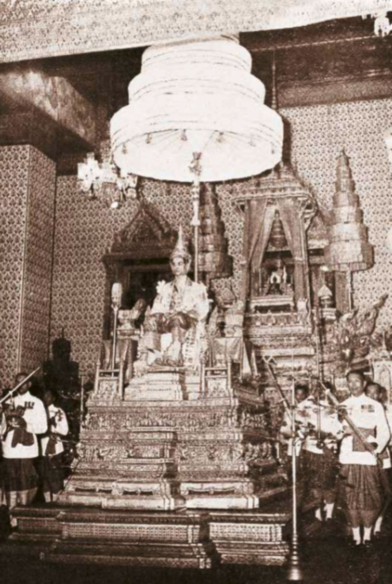 พระบาทสมเด็จพระปรมินทรมหาภูมิพลอดุลยเดช บรมนาถบพิตร ประทับพระที่นั่งพุดตานกาญจนสิงหาสน์ บนแท่นพระราชบัลลังก์ แวดล้อมด้วยเครื่องอิสริยราชูปโภค เสด็จออกมหาสมาคม ในการพระราชพิธีบรมราชาภิเษก ณ ห้องพระโรง พระที่นั่งอมรินทรวินิจฉัย