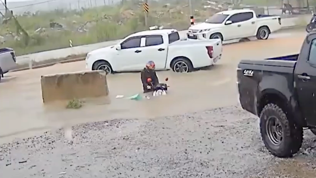 雨水泛滥骑摩托车的年轻人掉入没有盖子的排水沟